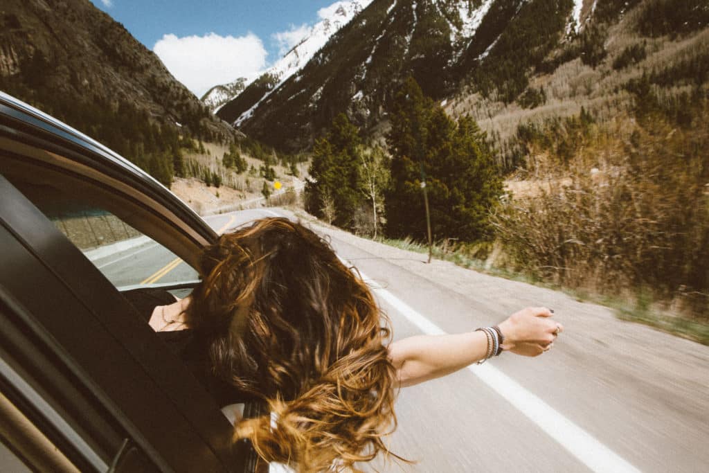 Woman enjoying the breeze while riding in the passenger seat through the mountains. 
