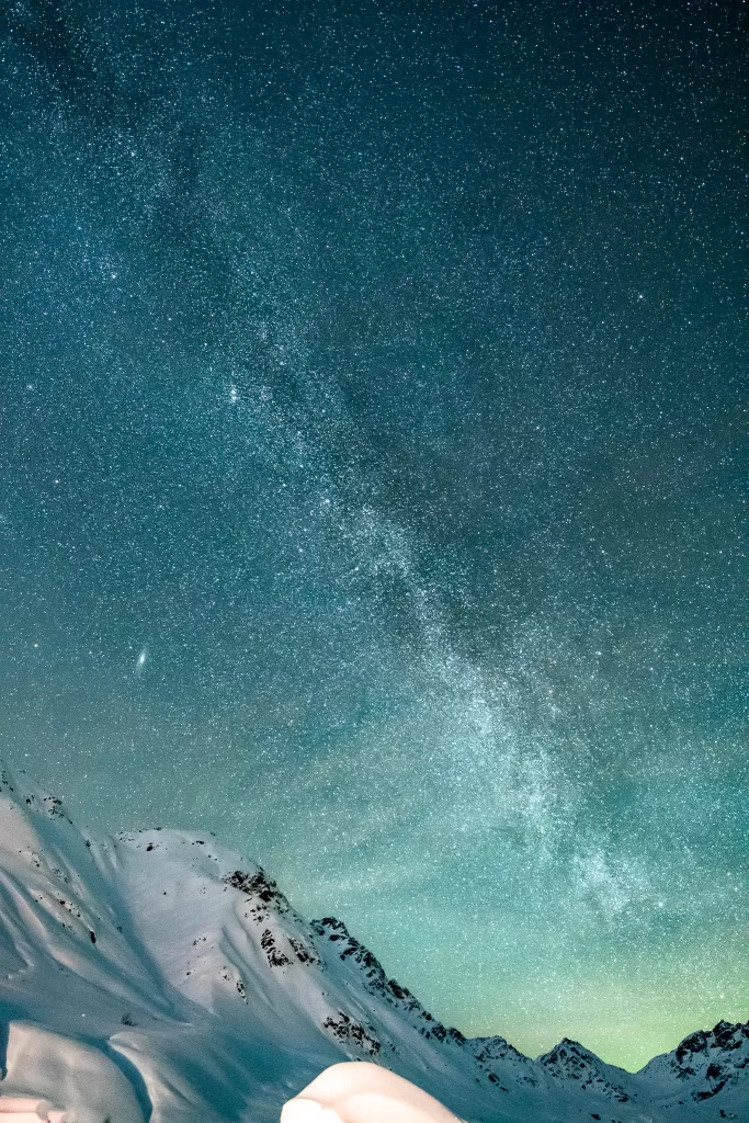 The Milky Way and a hint of the Aurora over snow-covered mountains during winter in Alaska. 