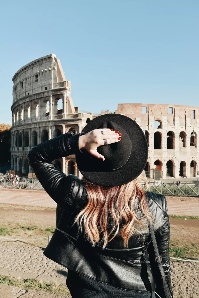 Girl at Colosseum in Europe with a black flat-brimmed hat and black jacket.