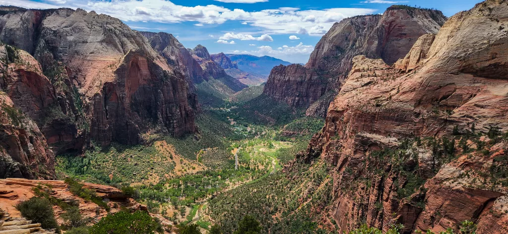 Zion Canyon from the perspective of Angel's Landing at the top during a clear summer day. The sandstone of Zion canyon is red and orange, contrasting against the green trees and shrubs in the valley and the blue sky. #Angel'slanding #Zionnationalpark #Zion #angel'slanding #angelslanding #zionhiking
